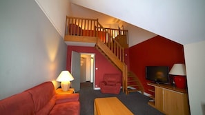 A living room with a red wall, a wooden staircase, a red sofa, a wooden coffee table, a TV, and a lamp. - Domaine DE LA Foret D Orient Natur Hotel Golf SPA (Rouilly-Sacey)