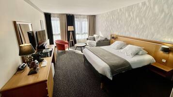 Een hotelkamer met een groot bed, een bureau met lamp, een televisie, een rode stoel en een bank.