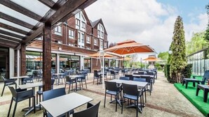An outdoor seating area with tables and chairs, a covered section with umbrellas, and a building in the background. - Domaine de La Foret D Orient Natur Hotel Golf Spa (Rouilly-Sacey)