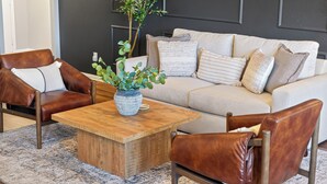 Un salon moderne avec un canapé beige, deux fauteuils en cuir, une table basse en bois et une plante en pot.