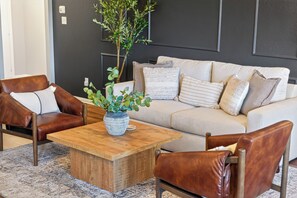 Ein modernes Wohnzimmer mit einem beigen Sofa, zwei Ledersesseln, einem Holztisch und einer Topfpflanze.