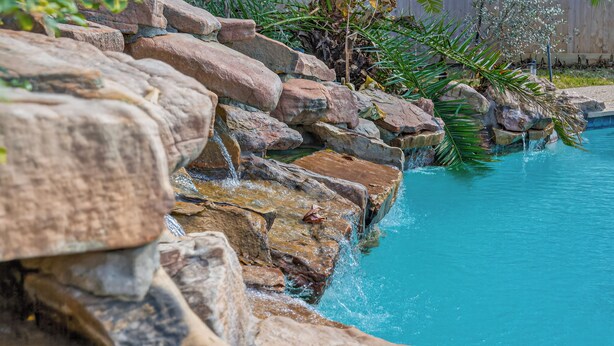 Une piscine agrémentée d’une cascade artificielle et entourée de verdure.