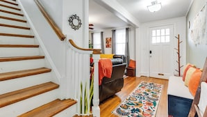 A staircase with wooden steps and white railings, a living room with a sofa and a colorful rug, and a door with a window.