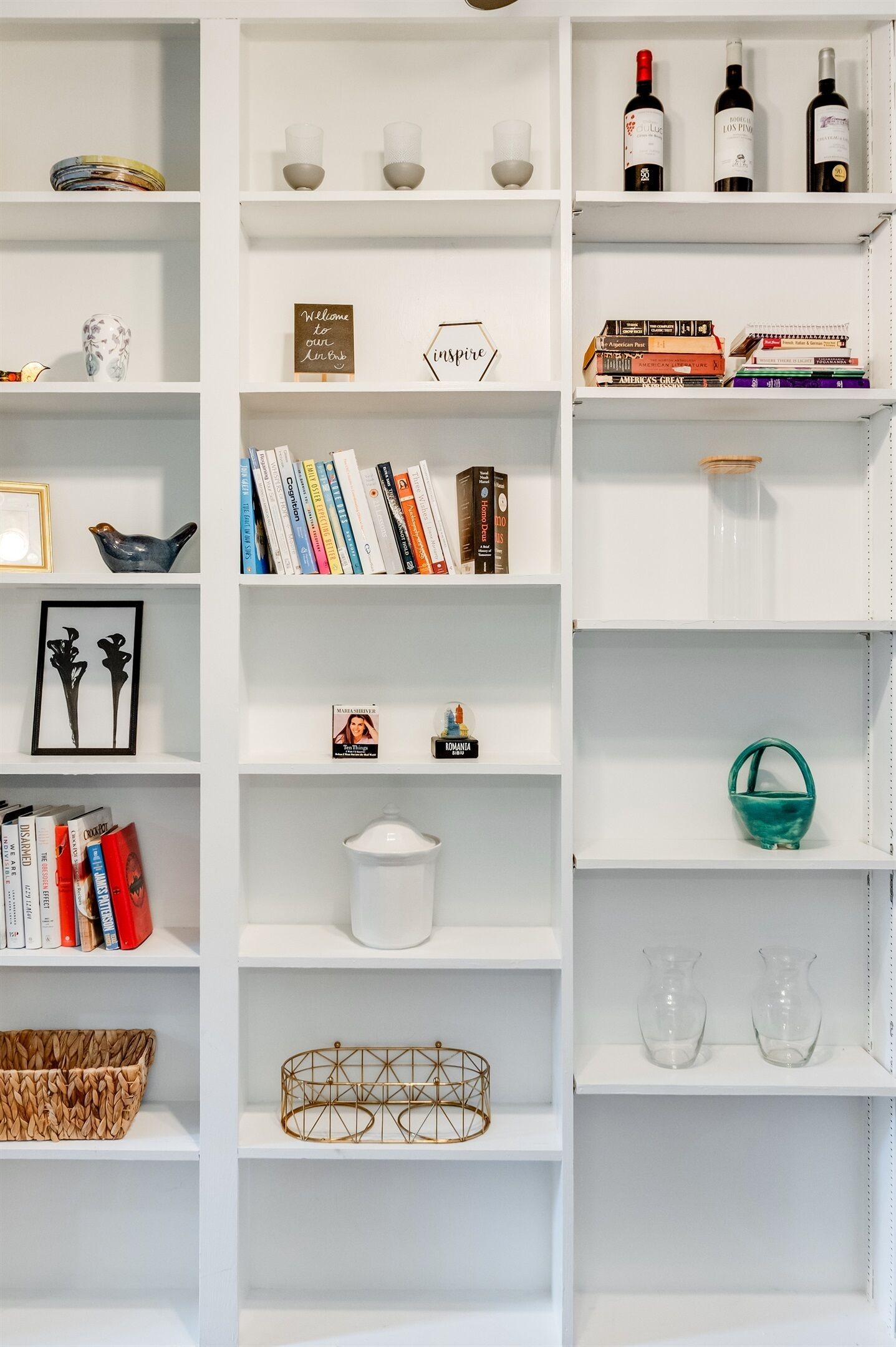 A white bookshelf with various items including books, decorative objects, and wine bottles.