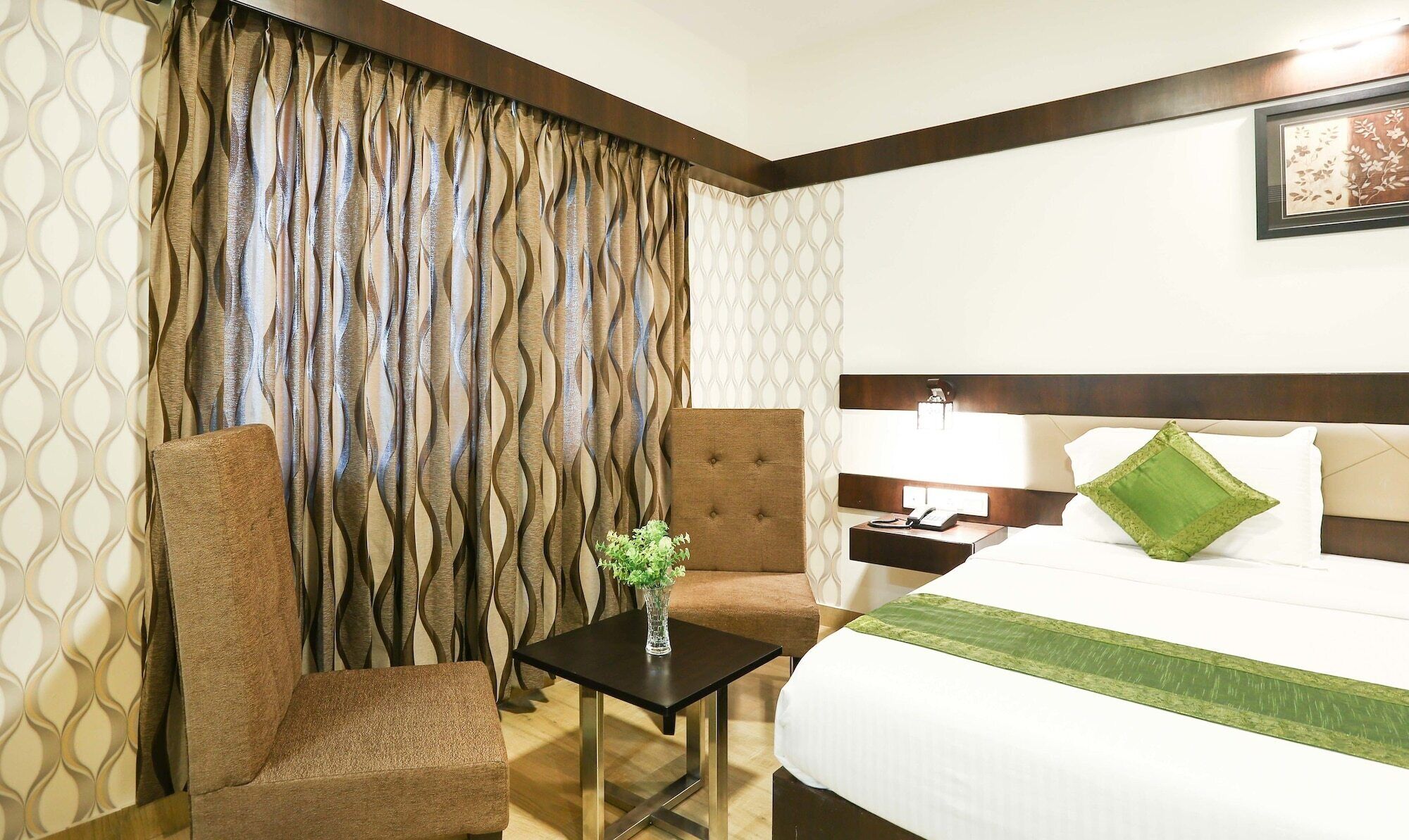 A hotel room with a bed, a nightstand, a lamp, a chair, and a small table with a vase of flowers.