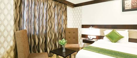A hotel room with a bed, a nightstand, a lamp, a chair, and a small table with a vase of flowers.
