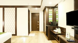 A hotel room with a wooden floor, a bed, a TV, a microwave, and a small table with a remote control. - Treebo Akshaya Mahal Inn (Mysore)