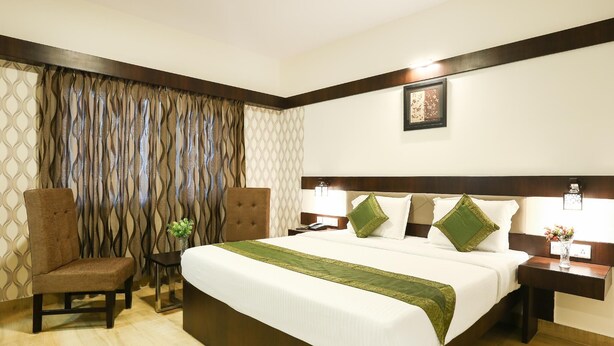 A hotel room with a large bed, two bedside tables, a chair, and a decorative wall panel. - Treebo Akshaya Mahal Inn (Mysore)
