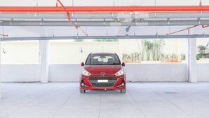 A red car parked in a spacious, well-lit parking garage with concrete floors and white walls. - Treebo Akshaya Mahal Inn (Mysore)