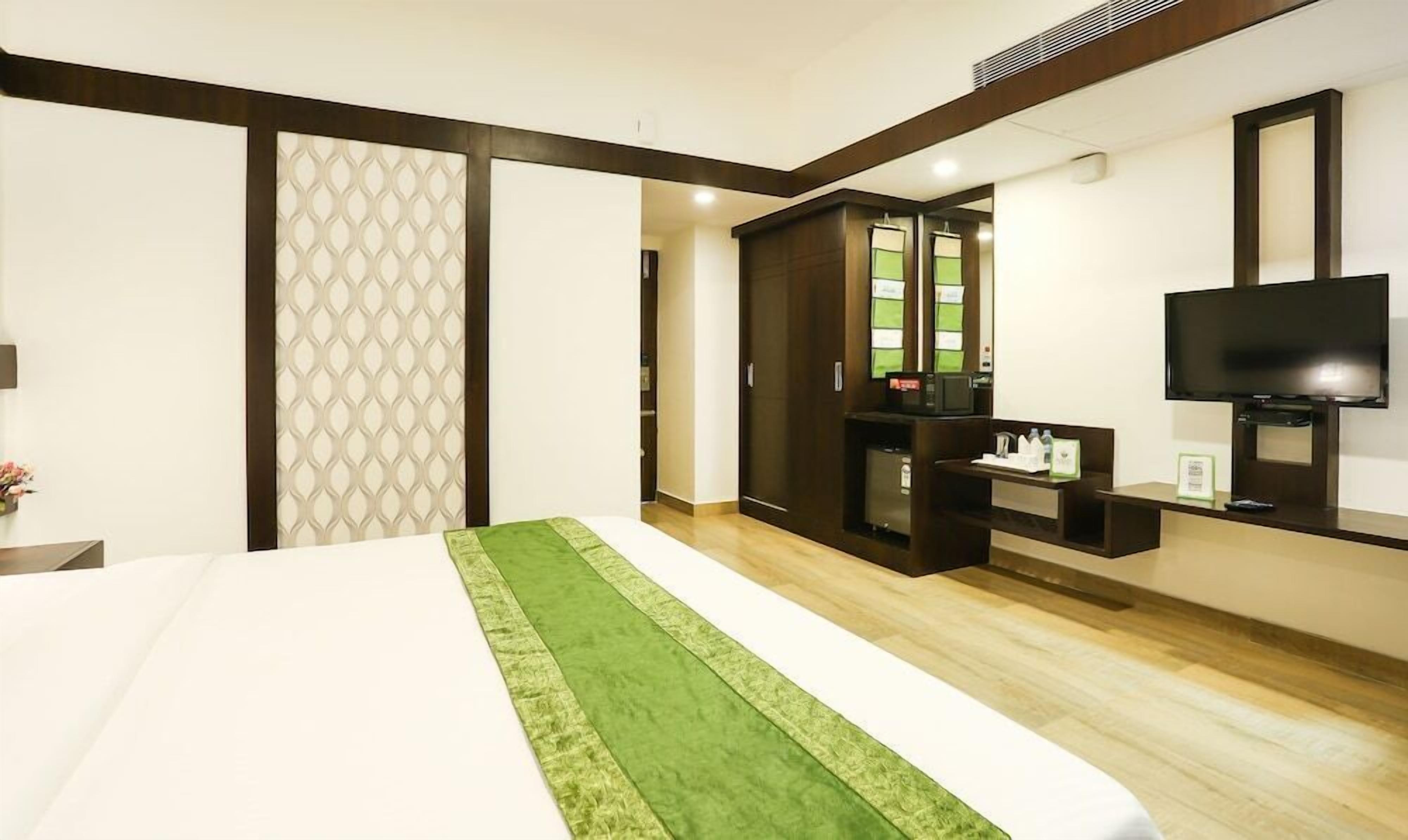 Habitación de hotel con cama, televisor, minibar y baño visible a través de una puerta de cristal.