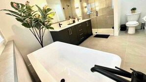 Un baño moderno con una bañera blanca grande, muebles oscuros y un espejo sobre el lavabo.
