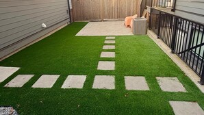 Ein Garten mit Kunstgrasanlage, Holzzaun und gepflastertem Weg.
