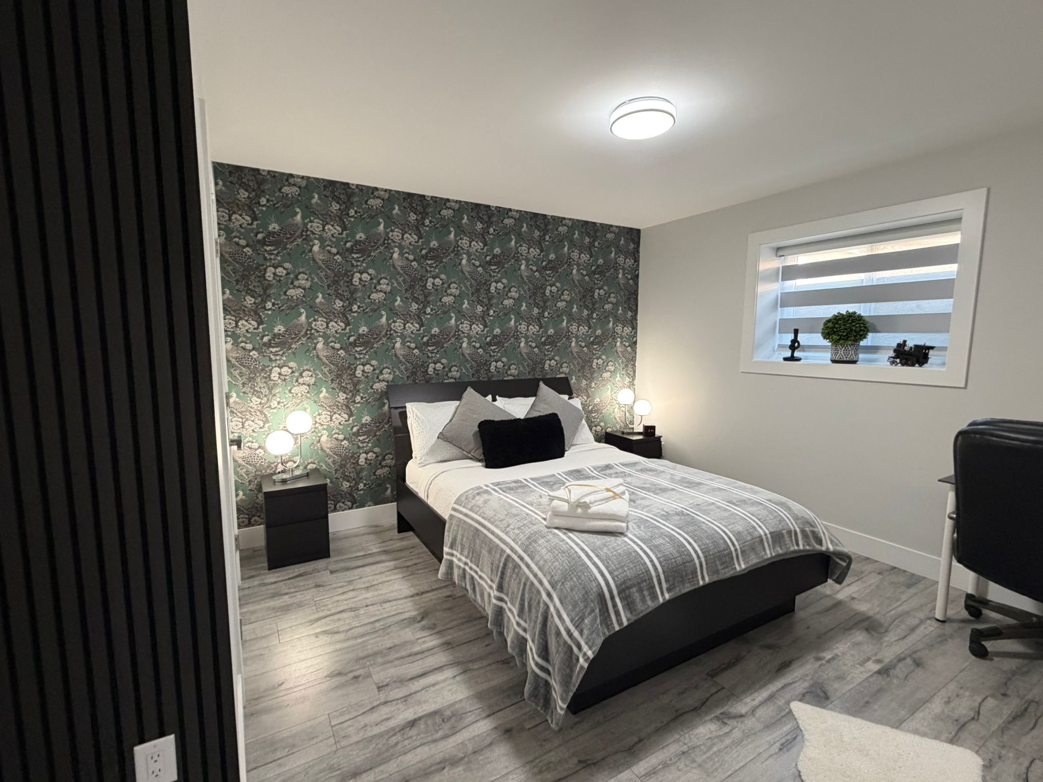 A bedroom with a bed, nightstands, a window with blinds, a desk, and a chair.