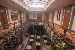 A restaurant with a high ceiling, wooden railings, and tables arranged around a central area. - Boutique B21 Malang, Azana Hotels Collection (Malang)
