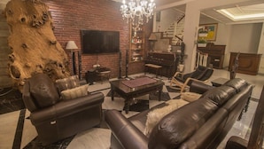 Un salon avec un mur en briques, une grande sculpture en bois, un lustre, des canapés en cuir, une table basse et un téléviseur à écran plat.