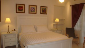 Un lit bien fait dans une chambre d’hôtel, avec une tête de lit blanche, deux tables de chevet avec des lampes et trois tableaux encadrés accrochés au mur.