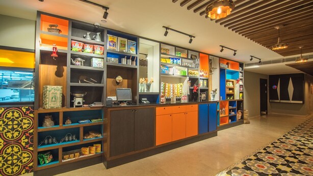 A brightly lit, modern hotel lobby with a central reception desk, colorful shelving units, and patterned floor tiles. - Zone By The Park Jodhpur (Jodhpur)