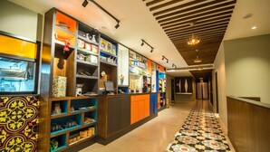 A hallway with a patterned floor, a reception desk with a computer, and shelves stocked with various items. - Zone By The Park Jodhpur (Jodhpur)
