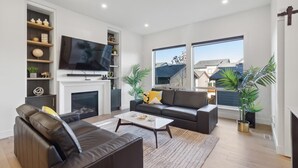 A modern living room with a fireplace, a large flat-screen TV, a sofa, and two potted plants.