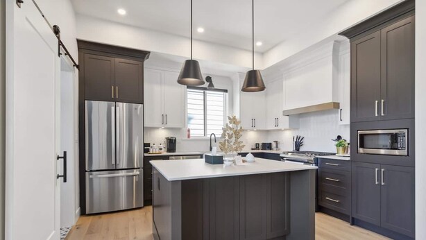 A modern kitchen with dark cabinetry, stainless steel appliances, and pendant lighting.