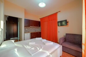 A bedroom with a bed, a sofa, a TV, and a kitchenette. - Melsi Apartments (Sarandë)