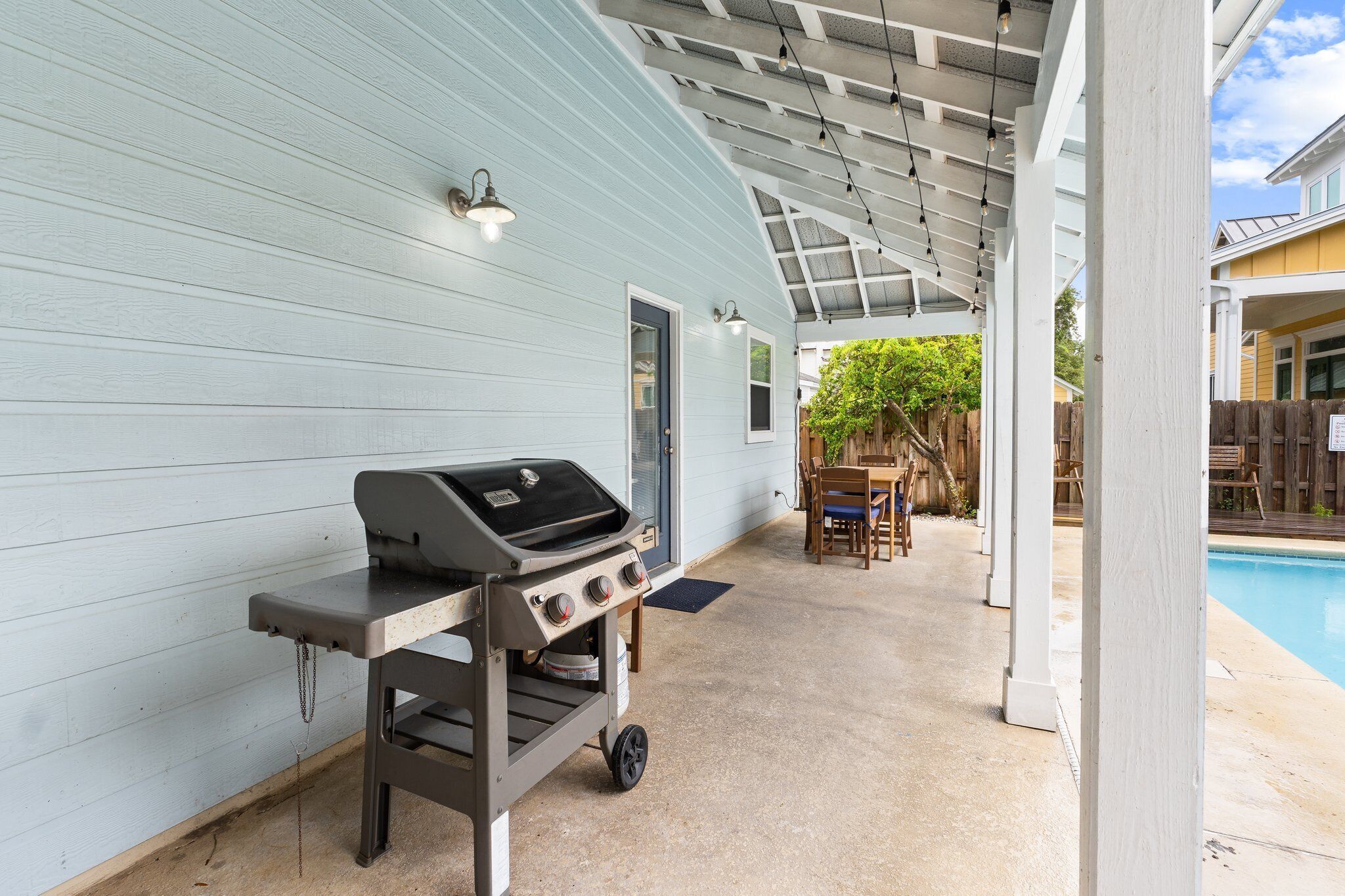 Ein überdachter Patio-Bereich mit Grill, Pool und Holzterrasse.