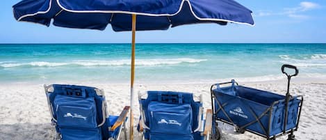 A beach scene with two beach chairs, a beach umbrella, and a beach wagon.