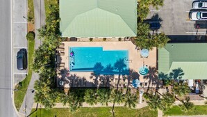 Vista aérea de un resort con piscina rodeada de palmeras y sillas de descanso.