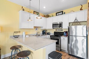 A kitchen with white cabinets, stainless steel appliances, and a central island with stools. - New! Crystal Beach Gem! Ocean View • Steps to Gulf • Caribbean Dunes 218 (Destin)