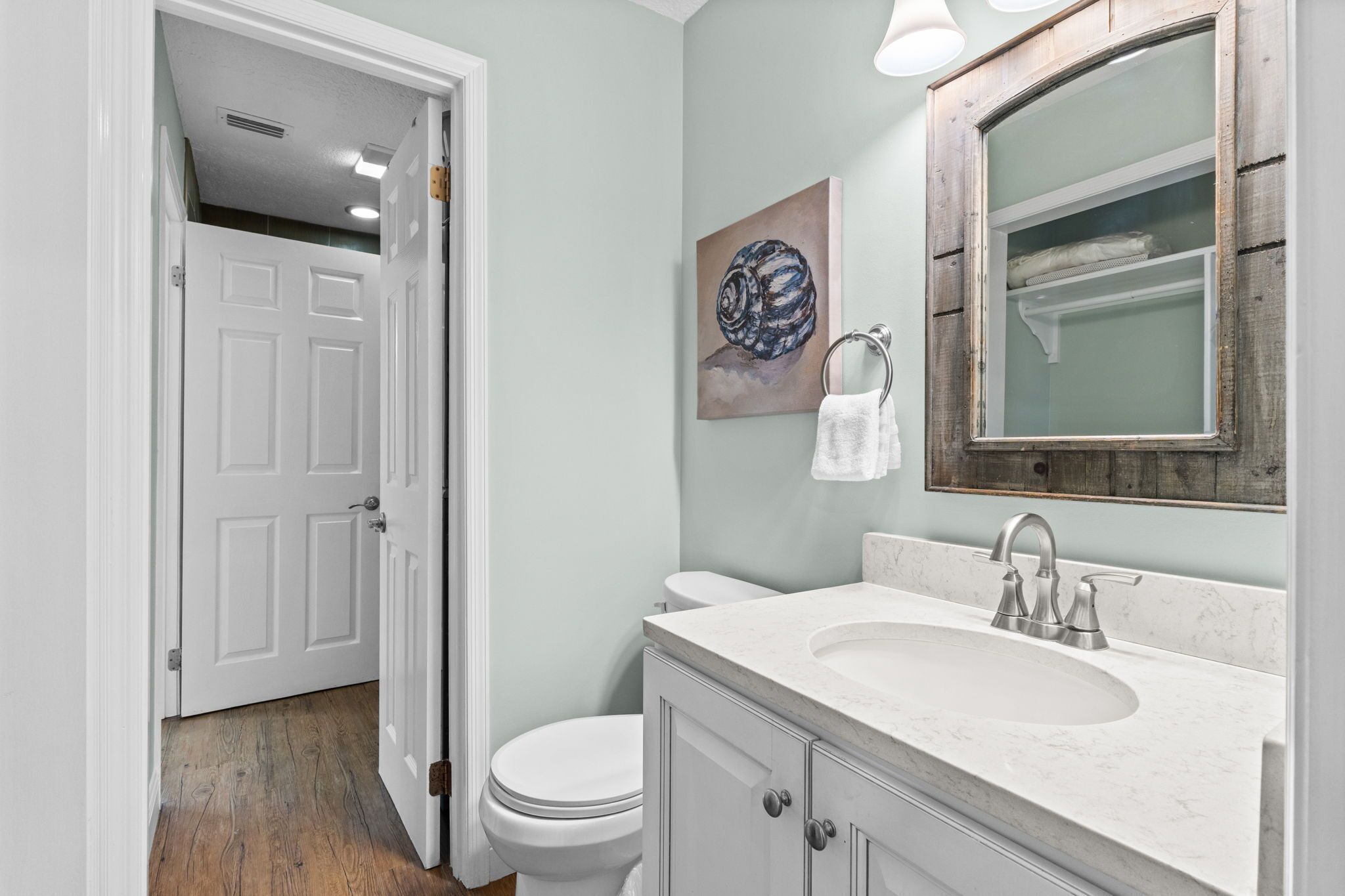 A bathroom with a white toilet, a sink with a marble countertop, and a wooden-framed mirror.