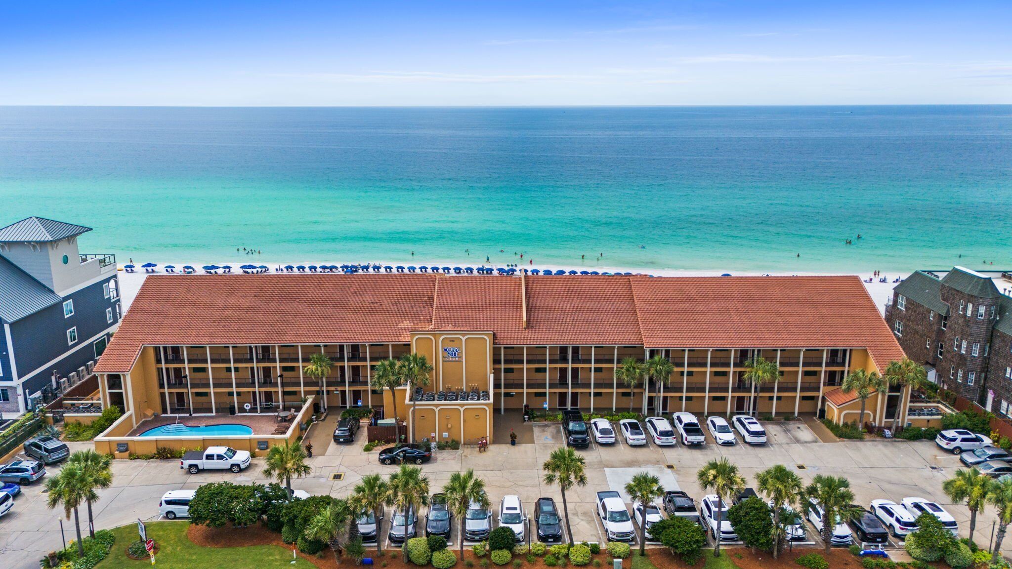 A hotel with a swimming pool, parking lot, and a view of the beach and ocean.