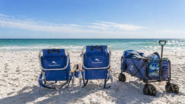 Twee strandstoelen en een bagagekar op een zandstrand, met de oceaan op de achtergrond.