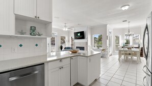 Een moderne keuken met witte kasten, een groot eiland en een eethoek met een kroonluchter.