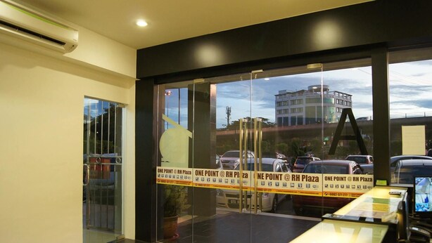 A modern hotel lobby with a glass door, a reception desk, and a view of the outside parking area. - One Point Hotel - RH Plaza (Kuching)
