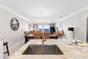 A modern kitchen with a marble countertop, stainless steel sink, and wicker furniture. - Beachfront~2 King Suites~Sunset Balcony~Family Resort w/Pool (Destin)