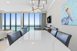 A modern conference room with a large table and leather chairs, large windows with a view of the ocean, a ceiling fan, and a painting of a pelican on the wall. - Beachfront Penthouse~Breath Taking Views~3 King Suites~2 Balconies! (Destin)