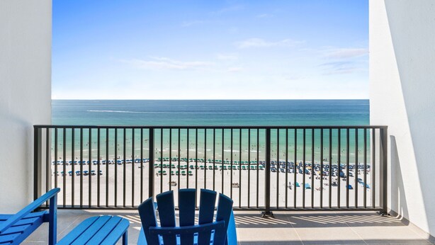 Ein Balkon mit Blick auf einen Strand, einem Geländer und blauen Stühlen.