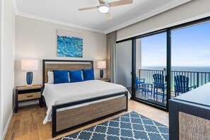 Une chambre d’hôtel moderne dotée d’un grand lit, d’un ventilateur de plafond, d’une vue sur l’océan et d’un balcon avec des chaises.