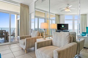 Ein Hotelzimmer mit einem großen Balkon, zwei gemusterten Sesseln, einem Sofa, einem Fernseher und einem Deckenventilator.