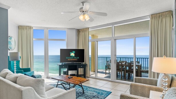 A spacious living room with a large TV, comfortable seating, a ceiling fan, and a view of the ocean through large windows. - Must See ! Beach Front~ 2 King Mstrs +2 Q Bdrm ~ Fantastic Views! (Destin)