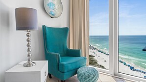Een smaragdgroene fauteuil bij een raam met uitzicht op het strand en de oceaan.