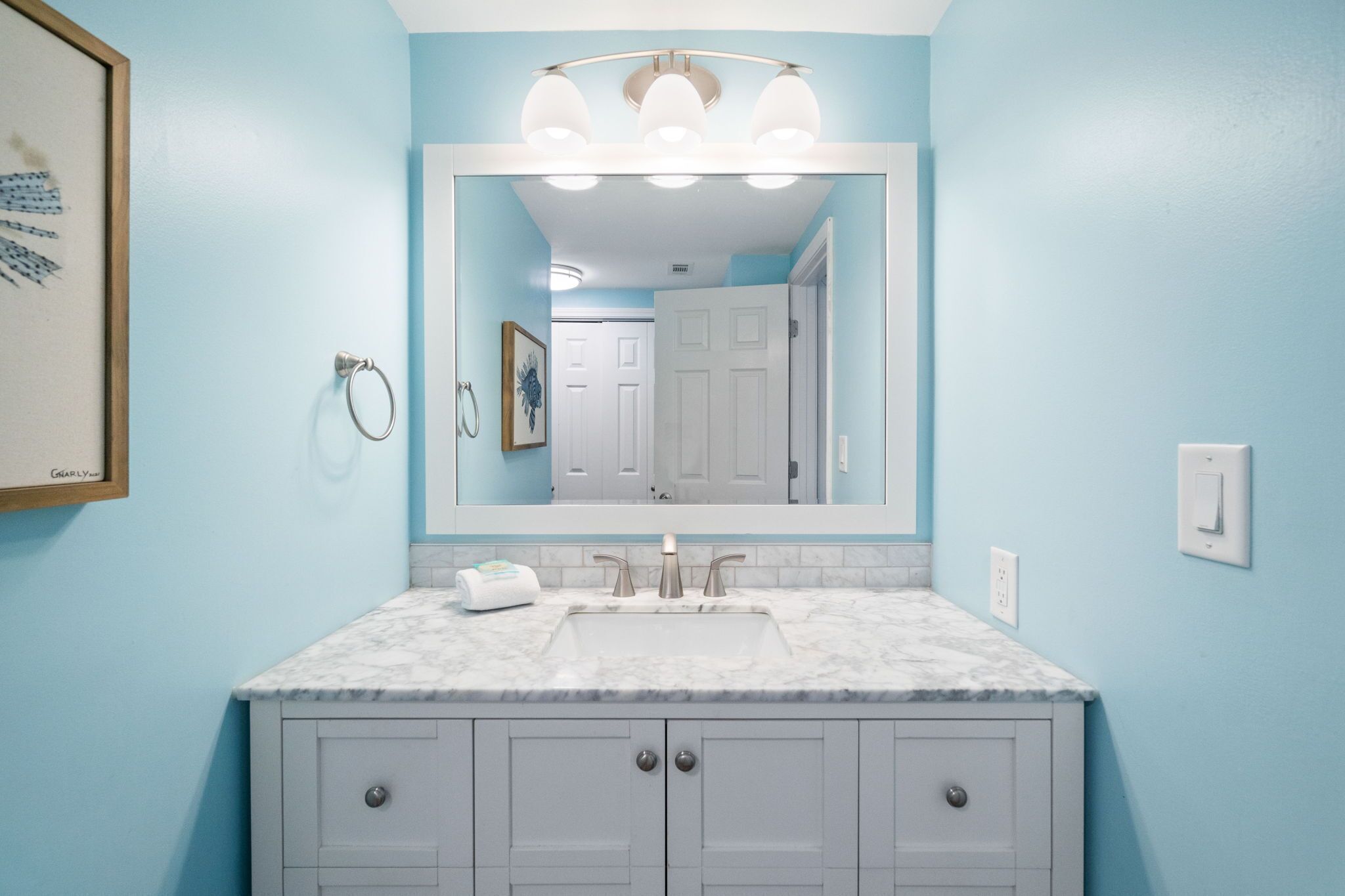 Un baño con lavamanos de mármol, un espejo grande y paredes azul claro.