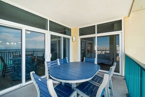 En balkon med et blåt bord og stole, store glasdøre og udsigt til havet.