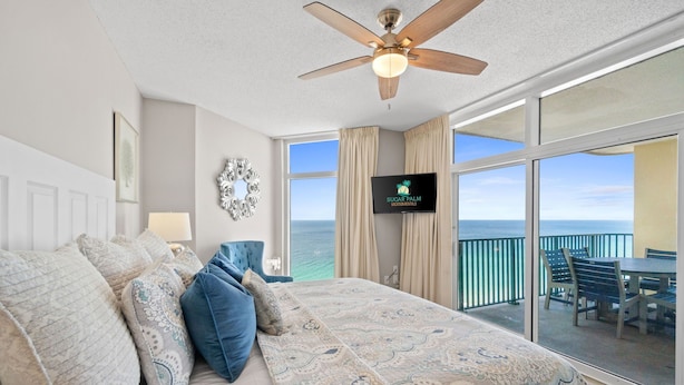 A bedroom with a large bed, a ceiling fan, a TV, and a balcony with a view of the ocean. - Upscale Condo with 2 King Master Suites and a 2-Queen Suite~ Wow Views! (Destin)