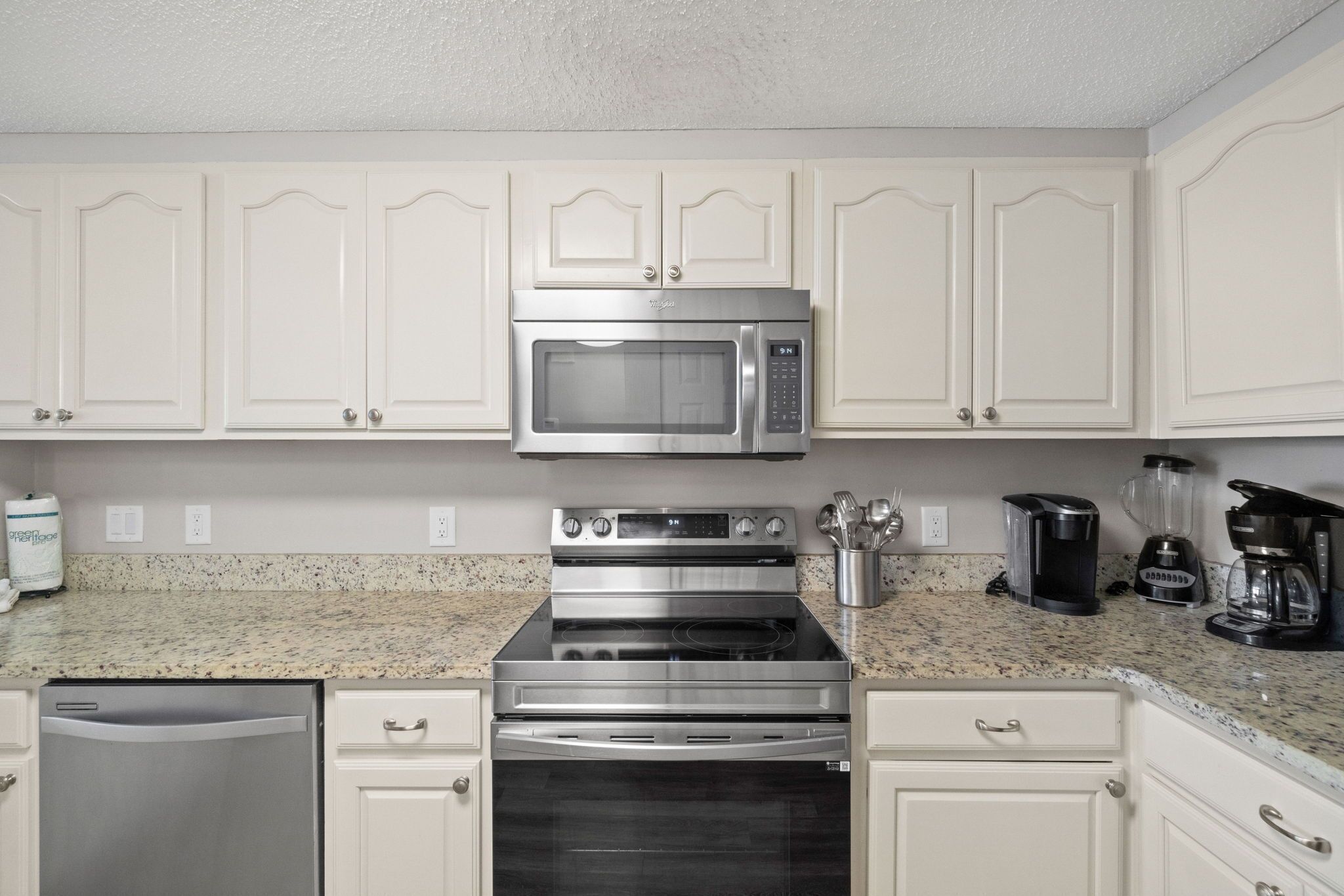 A kitchen with white cabinets, a stainless steel microwave, a stove, and a dishwasher.