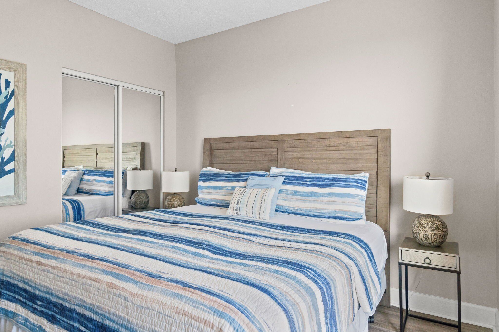 A bedroom with a large bed, two bedside tables with lamps, a mirror, and a wall-mounted artwork.