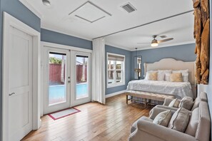 A bedroom with a large bed, a bench, a ceiling fan, and a view of the outside. - Carriage House~Beach Access~Private Pool~Pet Friendly~Beach Cottage (Destin)