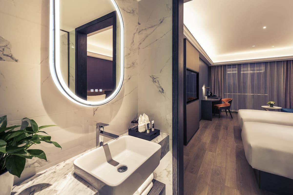 Un baño de hotel moderno con un lavamanos de mármol, un espejo grande con luz y una planta en maceta.
