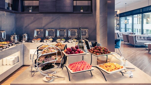 A buffet with various food items, a modern interior with a high ceiling, and a seating area with sofas and tables.