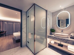 Un bagno moderno con doccia vetrata, un ampio specchio rotondo e un mobile lavabo in marmo.